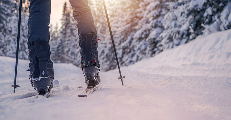 A person from the calf down wearing ski boots cross country skiing in powedery snow.