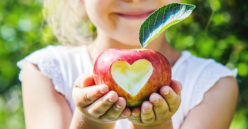 Apple with heart cut out of it being held by a little girl.