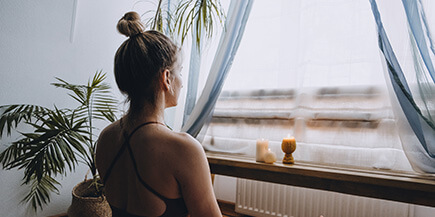 Woman sitting in front of a window with the curtains drawn in workout clothing.