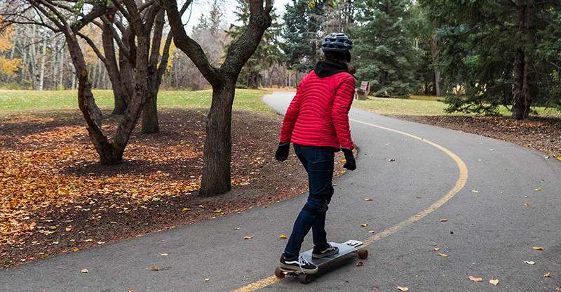 Woman riding a longboard down a path through a park