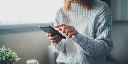 A woman in a sweater tapping a cellphone.