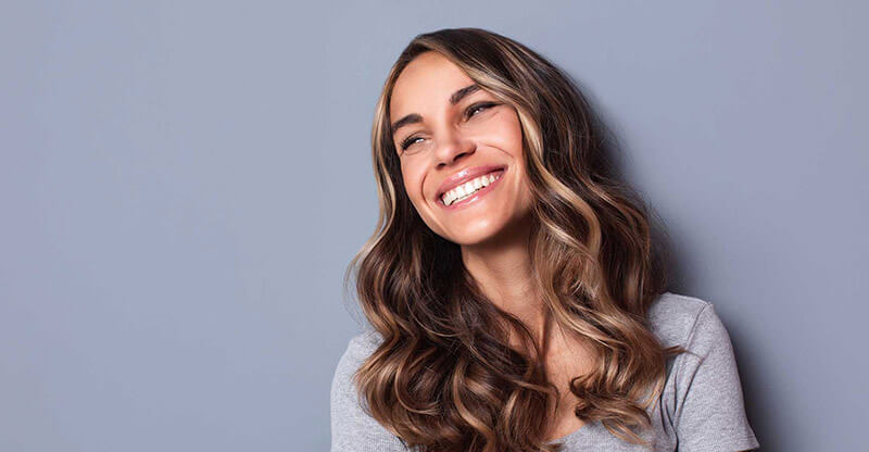 A woman with long curled hair smiles looking away from the camera.