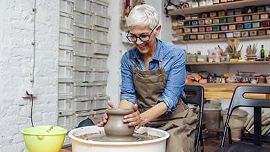 Senior female potter working on pottery wheel while sitting in her workshop