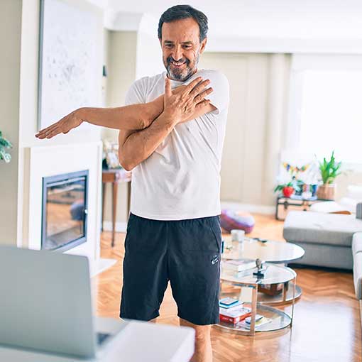 Person standing and stretching arm over chest while looking at a laptop.