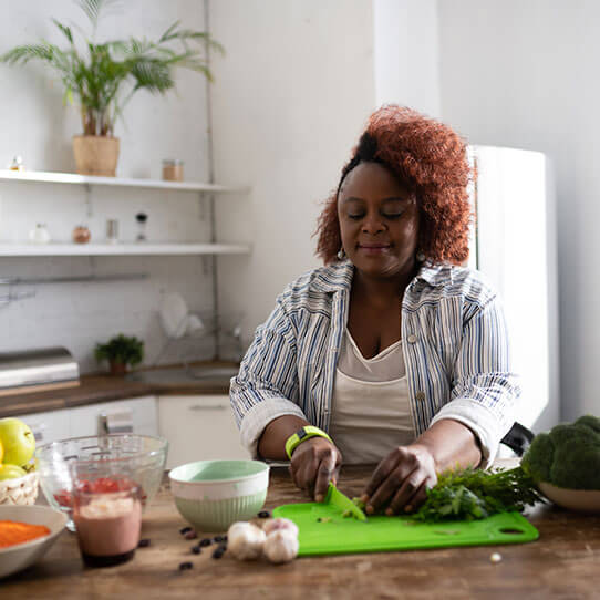 A middle-aged African-Canadian woman is preparing a salad in her kitchen. She is chopping fresh herbs to add to a bowl of vegetables.