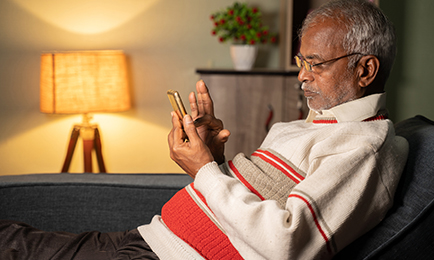 An elder Indian man sitting on the couch checking his phone