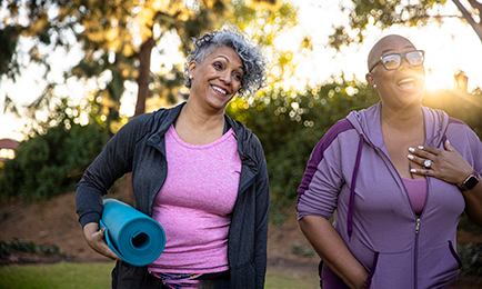 Two elder afroamerican women walking with a yoga mat and laughing