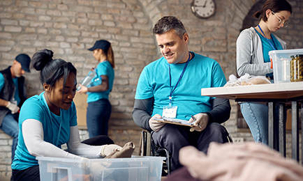 Happy volunteer coordinator in wheelchair supervising donation packaging at community center.