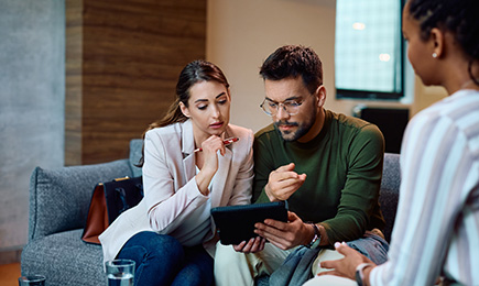 A man and two women sitting on a sofa looking at tablet with worried face.