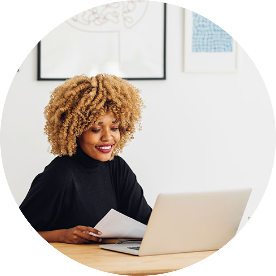 Woman smiling while holding papers and looking at a laptop.