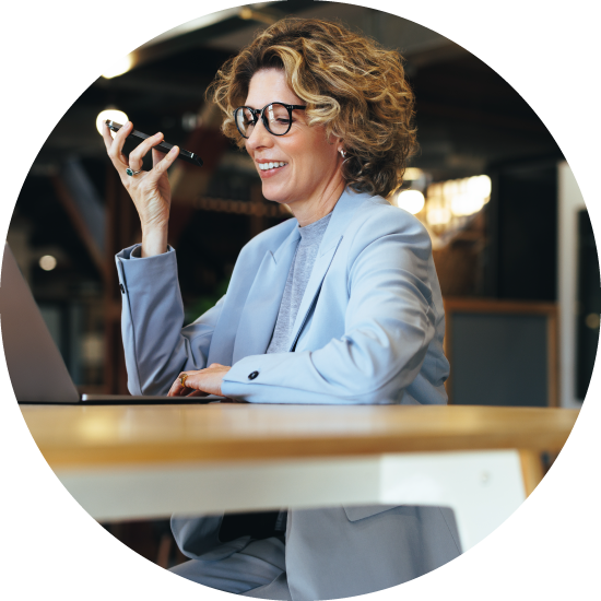 Woman in business suit and glasses talking into a mobile phone on speaker mode.