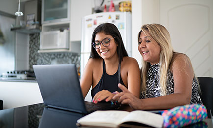 Mother and daughter chatting and smiling while filling out forms in computer.