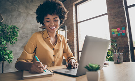 An african american woman happily working in fron of her computer.