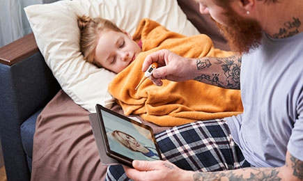 Dad taking care of daughter following instructions through a virtual consultation with a doctor