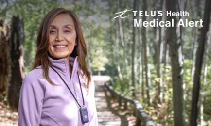 Woman smiling at camera while out on a walk wearing her TELUS pendant.