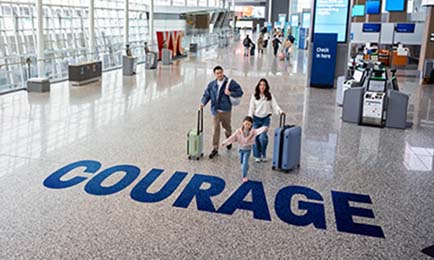 Family carrying luggage around the airport with the word courage on the floor.