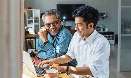 Two men smiling while using a laptop together