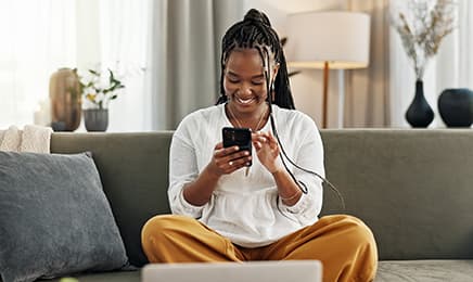 A lady sitting on the couch, smiling while using her phone.