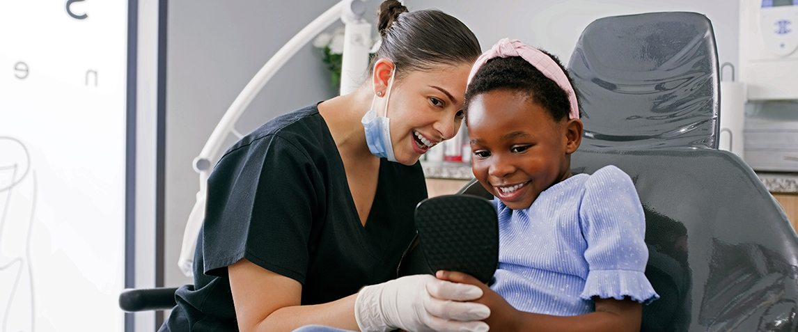 Photo of a smiling dentist with a young patient also smiling.