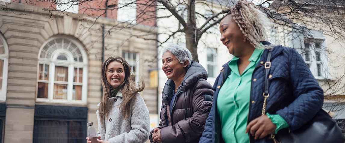 Photo of a three smiling women walking on the street.