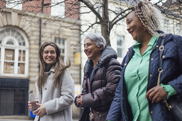 A shot of three females of varying ages walking home from work in the city. They are all wearing smart-casual clothing and laughing together.