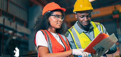 A man and a woman in hard hats and high visiblity vests consulting paperwork.