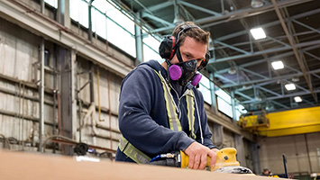 A man wearing ear protection and respirator while using electric sander.